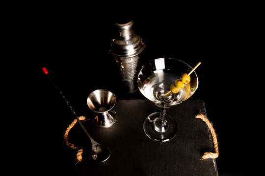 Close up of cocktail instruments and martini glass with three olives on black background. Zenith view