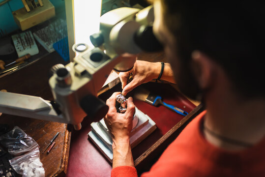 Unrecognizable jeweler hands working on a piece of jewelry at his workbench inside his workshop.