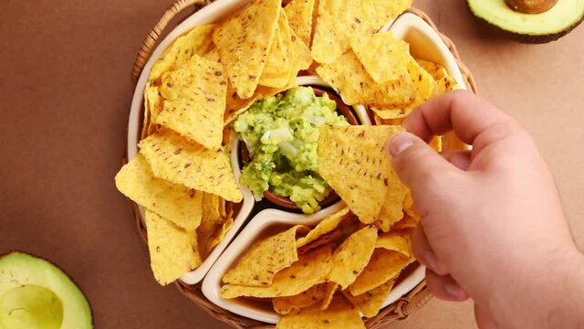 Hands taking some fried nachos in a pot with some fresh guacamole on a green surface 