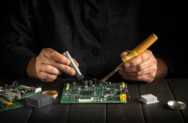 Electronic equipment repair service. Repair of electronic boards. A master with a soldering iron repairs equipment in workshop.
