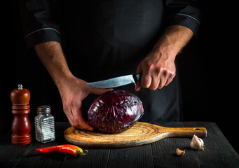Chef cutting red cabbage with a knife. Cooking vegetable salad in the restaurant kitchen. Vegetable diet idea.