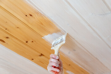 Young woman paints the wall with white paint.