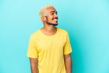 Young Colombian handsome man isolated on blue background looking side