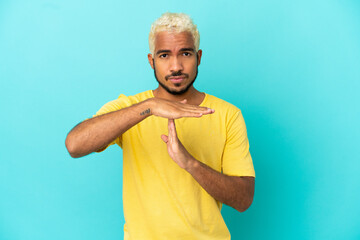 Young Colombian handsome man isolated on blue background making time out gesture