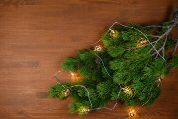 Christmas tree branch with lights on wooden background. Xmas and Happy New Year theme. Flat lay, top view. Copy space