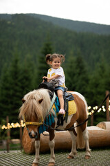 Pretty emotion baby girl riding a pony and smiling.