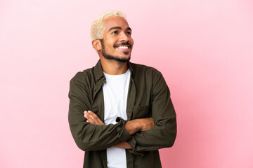 Young Colombian handsome man isolated on pink background looking up while smiling