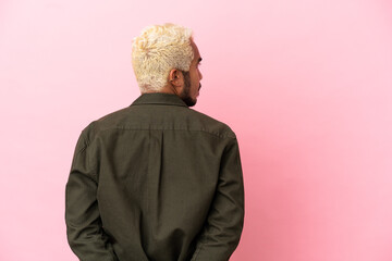 Young Colombian handsome man isolated on pink background in back position and looking back