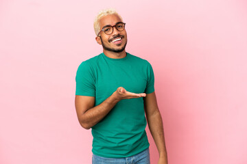 Young Colombian handsome man isolated on pink background presenting an idea while looking smiling towards