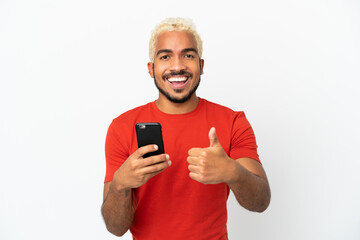 Young Colombian handsome man isolated on white background using mobile phone while doing thumbs up