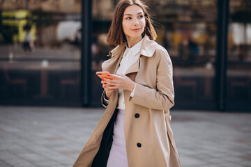 Fototapeta premium Young beautiful woman wearing coat walking in the city and talking on the phone