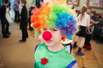 Portrait of boy in clown costume, colored wig and with red nose at party