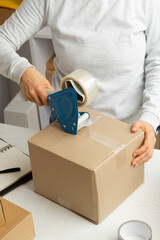 A warehouse worker packs a box of goods for delivery using an adhesive tape dispenser. - 474269239