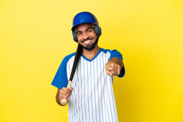 Young Colombian latin man playing baseball isolated on yellow background pointing front with happy expression
