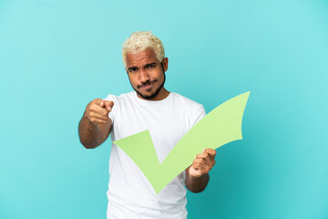 Young Colombian handsome man isolated on blue background holding a check icon and pointing to the...