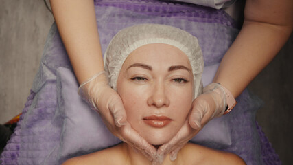 Woman receiving facial massage in spa salon on massage table. Wellness body and skin care, face...