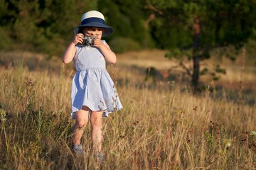  A little girl looks intently into the viewfinder of an old camera in nature. Selective focus. Copy  space.