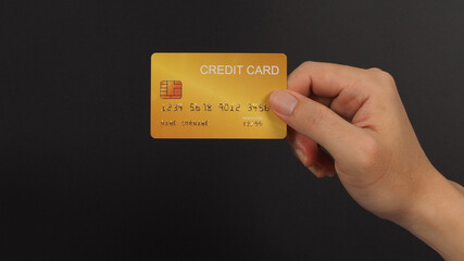 Gold color credit card in hand isolated on black background.
