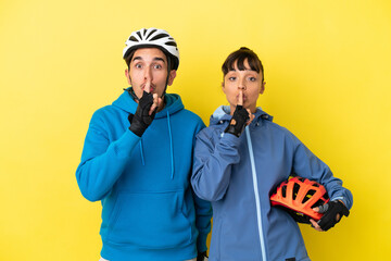 Young cyclist couple isolated on yellow background showing a sign of silence gesture putting finger in mouth