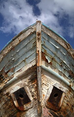 old abandoned wooden  boat close up against blue sky with clouds