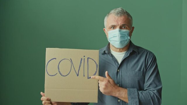 Portrait of a Frightened Man in a Medical Mask Holding a Sign With the Words 'COVID'. Pandemic, Covid 19 Global Conspiracy Theory, Medicine and Healthcare Services Concept.