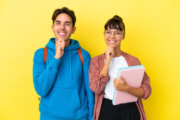 Young student couple isolated on yellow background smiling with a sweet expression