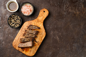 A piece of cooked beef meat steak on wooden board cut in slices, white and black peer, coarse sea salt. Top view, negative space