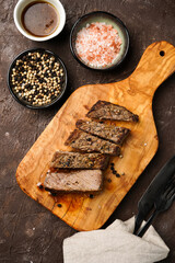 A piece of cooked beef meat steak on wooden board cut in slices, white and black peer, coarse sea salt, top view