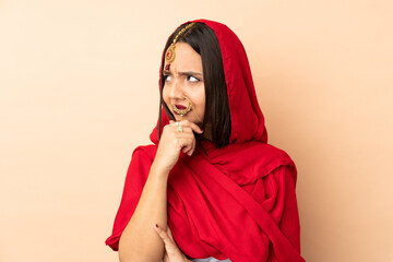 Young Indian woman isolated on beige background having doubts and with confuse face expression
