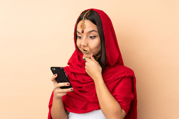 Young Indian woman isolated on beige background thinking and sending a message