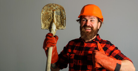 Smiling builder in hardhat with shovel shows thumb up. Workman in work gloves with spade. Copy...