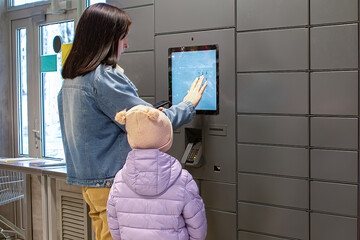Mom and daughter receive their order, their purchases via the Internet in a self-service parcel machine, they dial the confirmation number from the phone and wait for the cell to open.