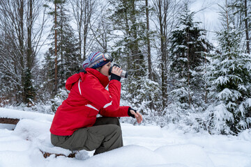 Caucasian woman in winter forest. Girl enjoys the snow falls. Young girl drinking tea in the forest during a snowfall. Have a good time outdoor in a snowy forest. Attractive young woman in forest