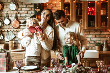 family of four parents pregnant mom and dad and two siblings little boy and girl in stylish clothes in chalet are ready to welcome Christmas and New Year at set table for festive dinner
