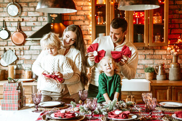family of four parents pregnant mom and dad and two siblings little boy and girl in stylish clothes in chalet are ready to welcome Christmas and New Year at set table for festive dinner