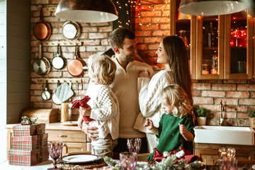 family of four parents pregnant mom and dad and two siblings little boy and girl in stylish clothes in chalet are ready to welcome Christmas and New Year at set table for festive dinner