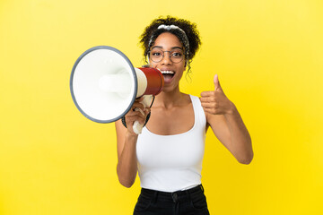 Young african american woman isolated on yellow background shouting through a megaphone to announce...