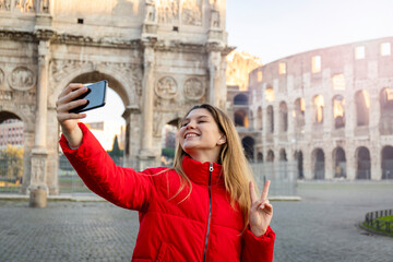 Young charming woman making a selfie in front of the Colosseum during a winter vacation. Lovely memories to be cherished.