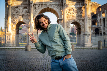 Happy moment in Rome. Young smiling man posing for a picture doing the V sign in front of the Titus arch.