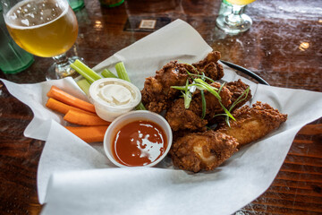 Close up of deliciously golden and fried chicken wings in a basket, next to cups of ranch and hot...