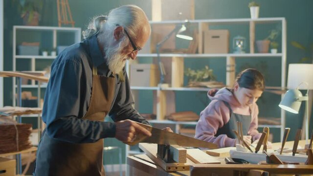 Grandfather Carpenter with his Teenage Granddaughter Work on Wood With Carpentry Tools in the Workshop. Communication of Generations, Training in the Craft. Concept of Handmade, Profession and Family.
