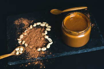 Low key high contrast carob/cocoa peanut butter jar with heart from peanuts on a black stone slate and black background