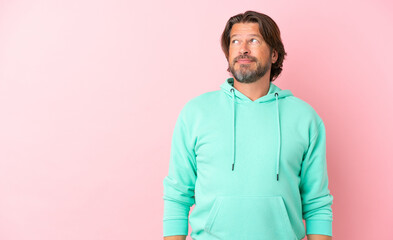 Senior dutch man isolated on pink background making doubts gesture looking side