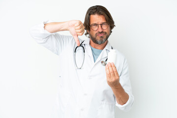 Senior dutch man isolated on white background wearing a doctor gown and holding pills while doing bad signal