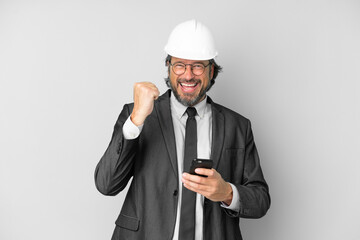 Young architect man with helmet over isolated background with phone in victory position