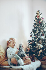 Little girl - toddler - playing with toys and decorations sitting next to a Christmas tree