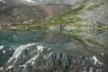Snowy mountain reflected in clear water of glacial lake. Beautiful sunny landscape with snow-white glacier reflection in water surface of mountain lake. White snow on rock reflected in mountain lake.