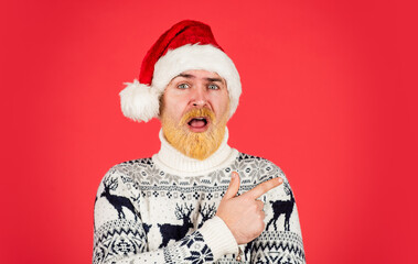 Feast of Christmas. christmas shopping time. mature male knitted xmas sweater. brutal man hate winter holidays. surprised man santa hat. bearded hipster dyed hair red background. new year party