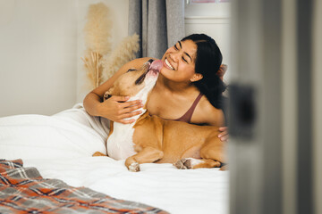 Dog Licking Face Of Smiling Woman On Bed