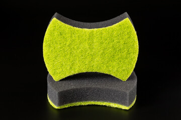 Two black sponges with an abrasive bright green layer for washing dishes and other domestic or household needs are isolated on black background